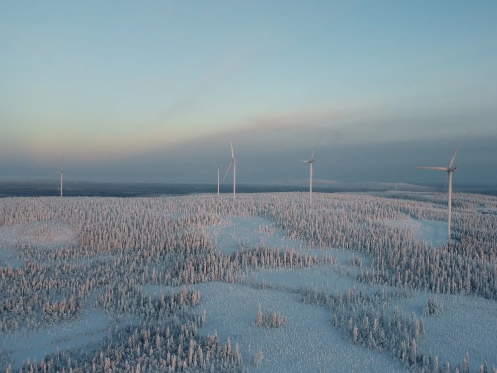 Verschneite Landschaft mit vier Windrädern unter klarem Himmel.