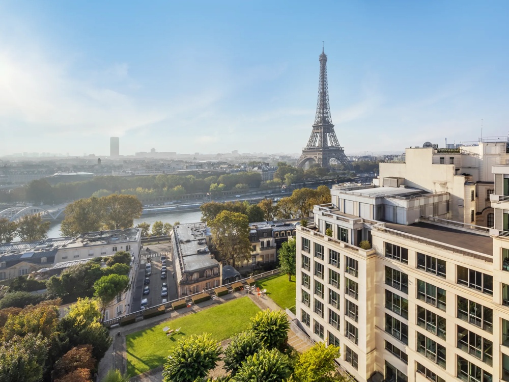 Blick auf den Eiffelturm über die Seine, umgeben von Bäumen und Gebäuden bei klarem Himmel.