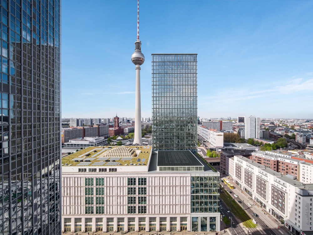 Moderne Hochhäuser und Fernsehturm überblicken eine belebte Stadtstraße bei klarem Himmel.