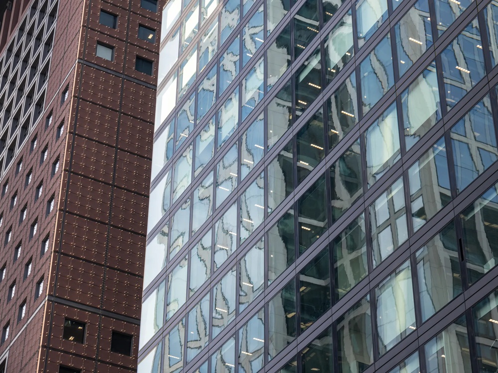 Moderne Glasfassaden von zwei Hochhäusern mit reflektierenden Fenstern und geometrischen Mustern.