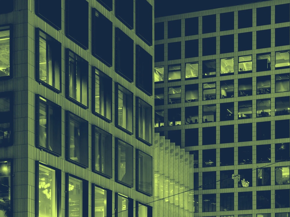 Moderne Gebäude mit vielen erleuchteten Fenstern bei Nacht, geometrische Strukturen und rechteckige Muster.