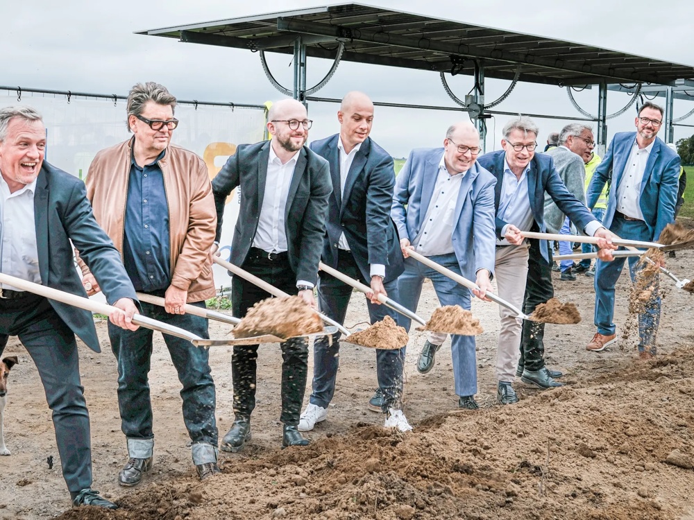 Acht Männer in Anzügen heben mit Schaufeln Erde auf einer Baustelle.