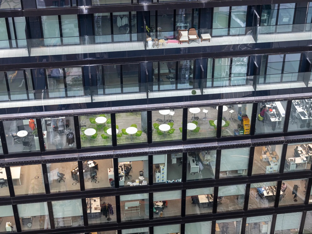 Bürogebäude mit Glasfassade zeigt leere Büros, Besprechungsräume und grüne Stühle um weiße Tische.