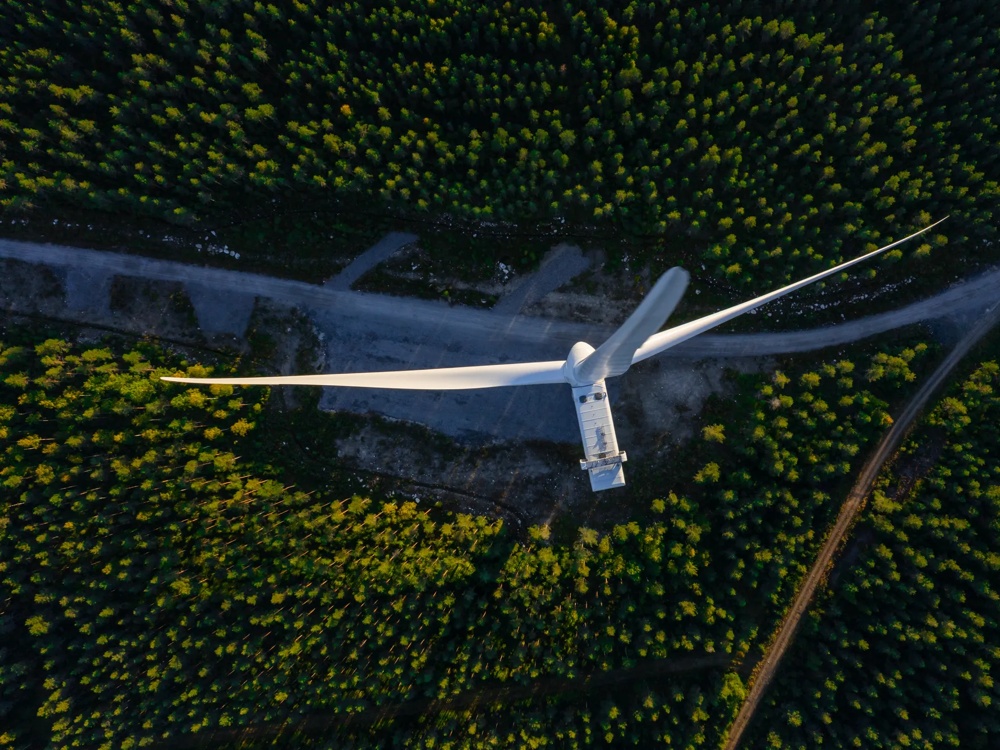 Windturbine von oben, umgeben von dichtem Wald und einem schmalen Weg.