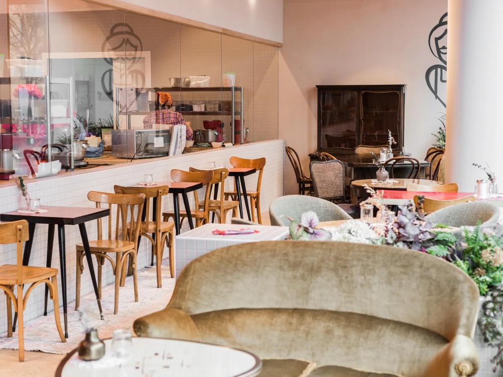 Gemütliches Café mit Holzmöbeln, Theke mit Barhockern, Pflanzen und dekorativen Elementen.