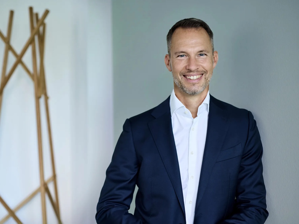 Michael Henn ist Global Head of Green Deal Infrastructure. Michael Henn lehnt gegen eine gruene Wand, neben ihm ist eine Metall-Skulptur.