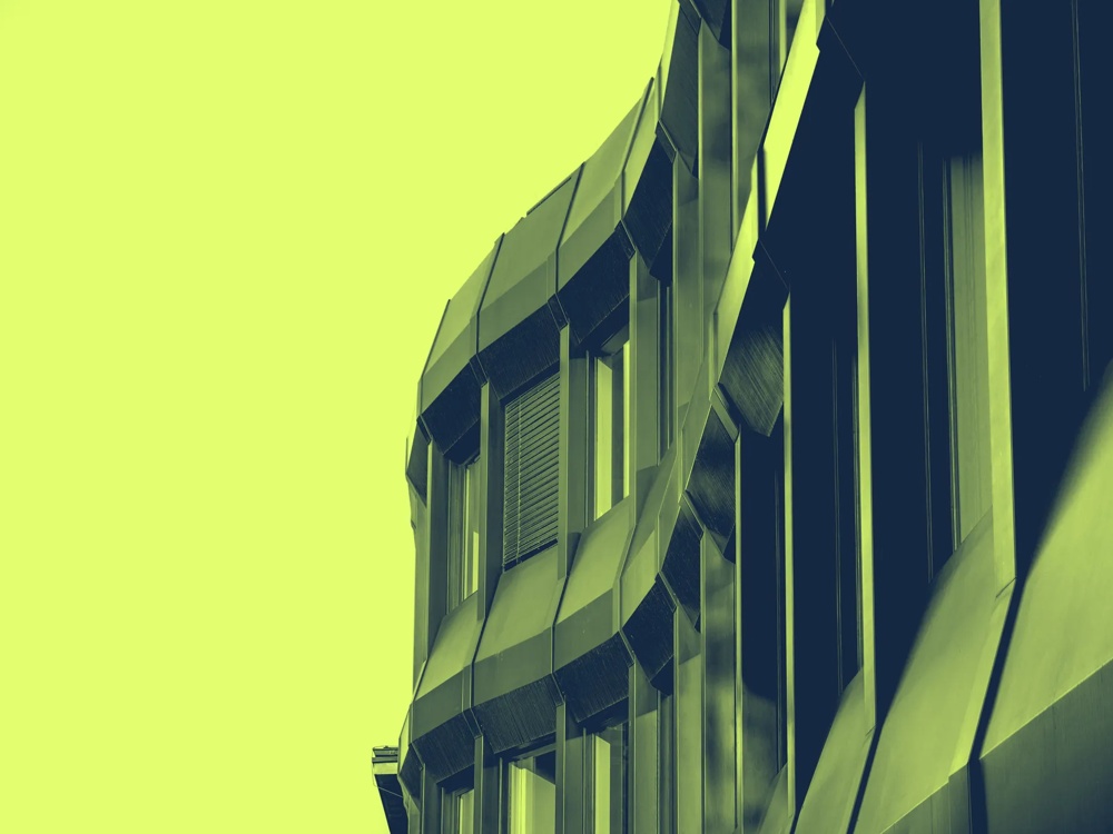 Futuristische Fassade eines Gebäudes mit welligen Metallverkleidungen und großen Fenstern, in gelb-grüner Tönung.