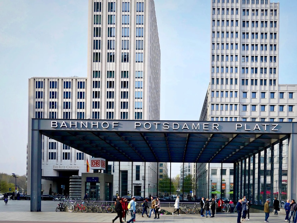Eingang Bahnhof Potsdamer Platz, moderne Gebäude, Menschen und Fahrräder im Vordergrund.