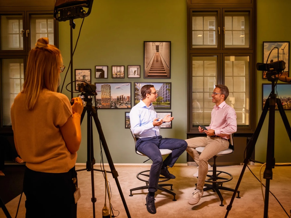 CEO Henning Koch und Pressesprecher Maurice Farrouh im Gespraech vor der Kamera im hauseigenen Fernsehstudio der Commerz Real. Es sind eine Vielzahl von Kameras zu sehen und eine Kamerafrau, die das Gespraech aufzeichnet.