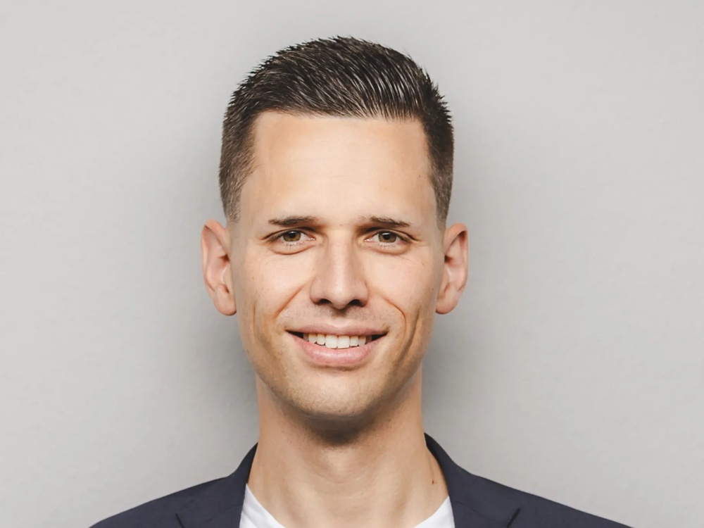 Zu sehen ist ein junger Mann im Porträt mit weißem T-Shirt mit schwarzen Sakko