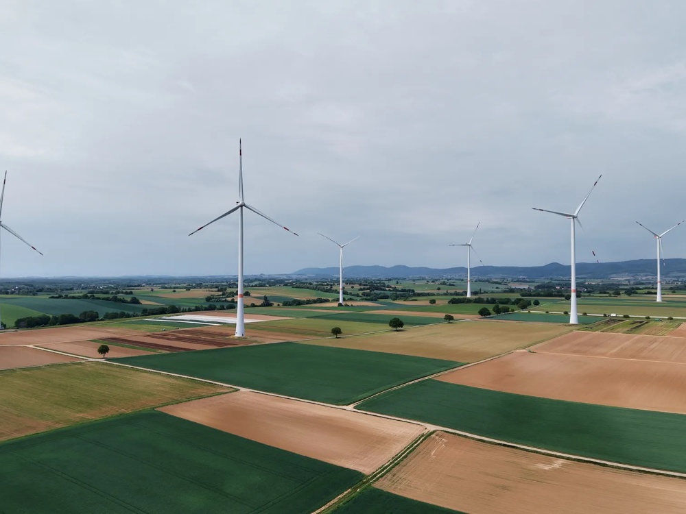 Windräder stehen auf weiten Feldern unter einem bewölkten Himmel bei Sonnenuntergang.