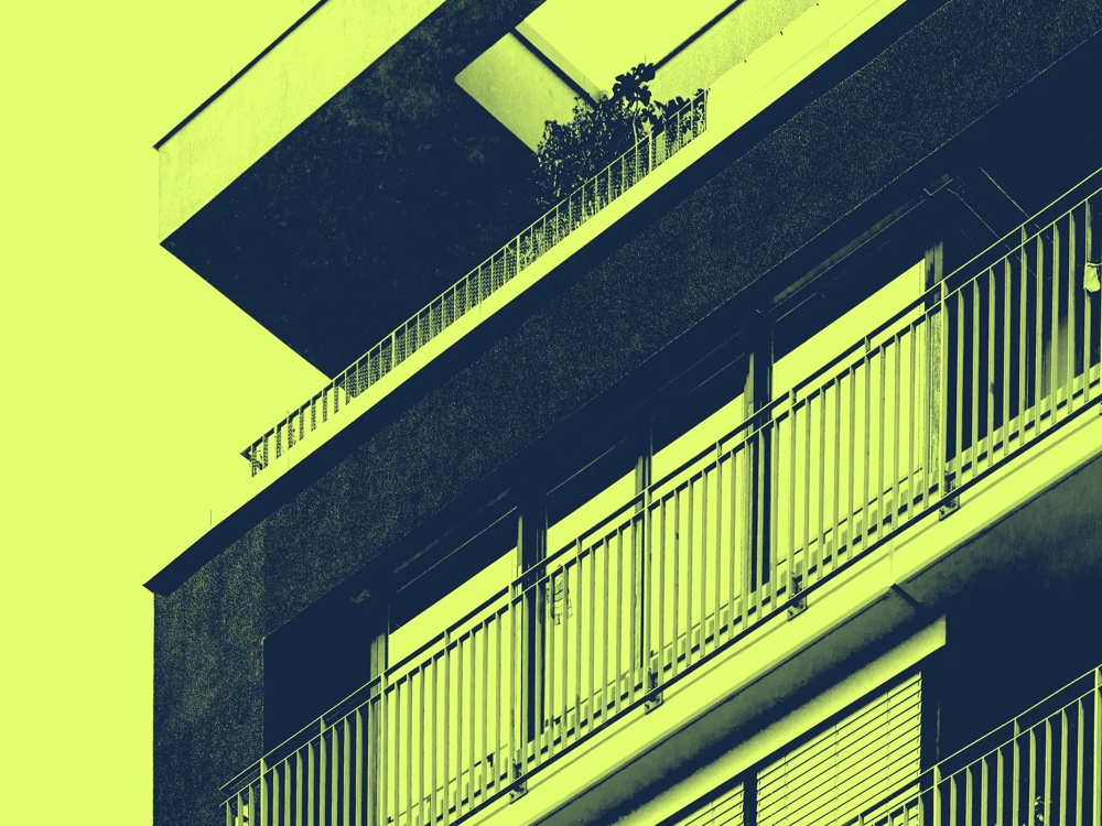 Ein modernes Gebäude mit Balkonen in gelb-grüner Farbgebung, Pflanzen auf dem oberen Balkon.