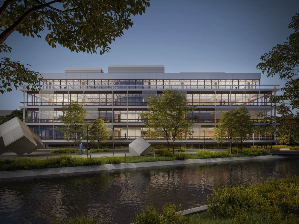 Ein modernes, verglastes Gebäude mit Bäumen davor, reflektiert im Wasser eines Kanals bei Dämmerung.