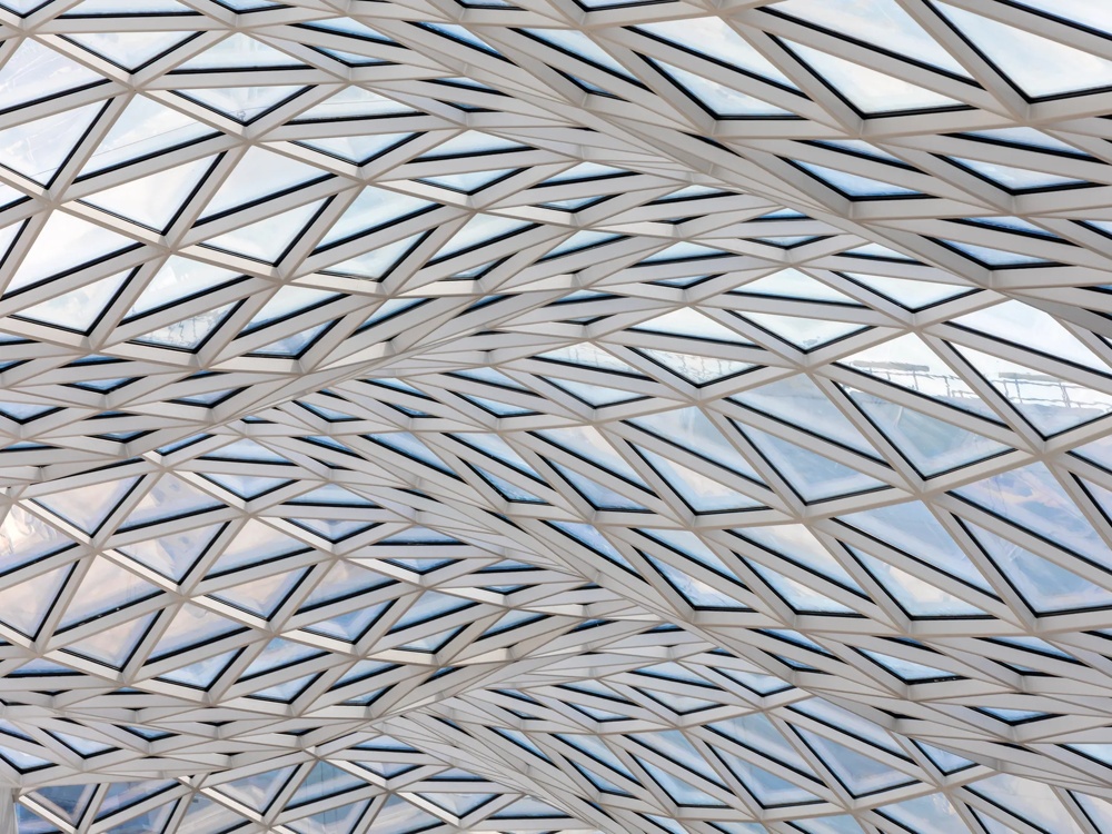Glasdach mit geometrischem Muster aus dreieckigen Paneelen und wellenförmigen Schatten.