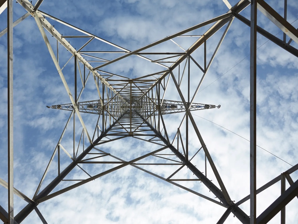 View from below through a power tower into the blue sky with white clouds.
