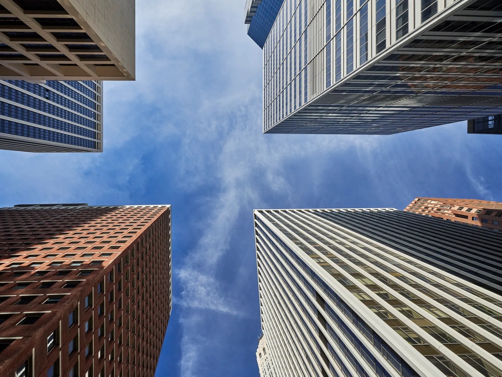 Upward view of four skyscrapers framing the blue sky.