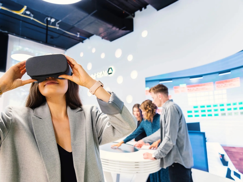 Zu sehen ist eine Frau im Vordergrund, die durch eine VR-Brille guckt.