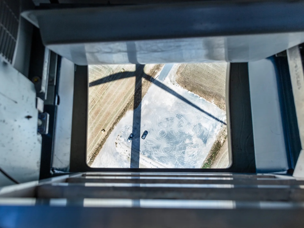 Eine Person steht auf einer Windkraftanlage und schaut auf ein Gerät, mit mehreren Windrädern im Hintergrund.