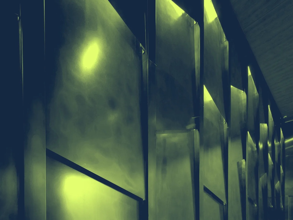 Metallische Wand mit geometrischen Paneelen, beleuchtet von gelbem Licht, erzeugt eine futuristische Atmosphäre.