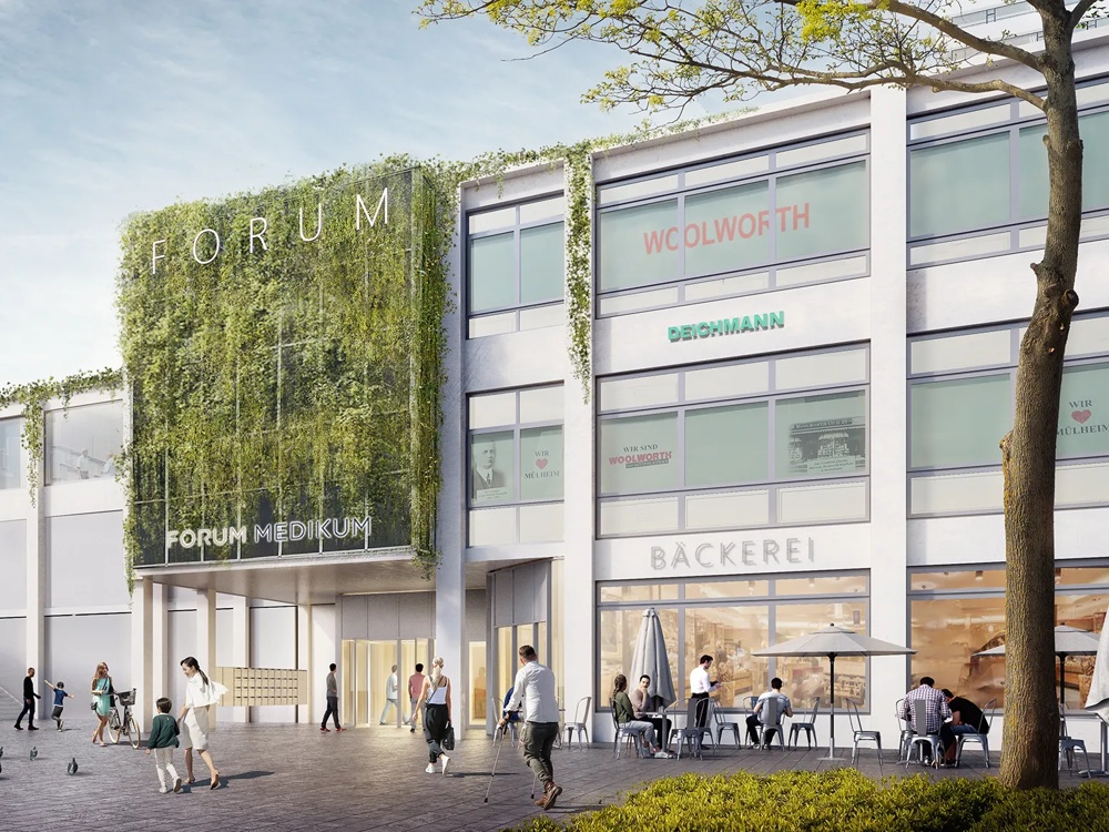 Moderne Gebäude mit begrünten Fassaden, Menschen spazieren und radeln, Tauben auf dem Platz, blauer Himmel im Hintergrund.