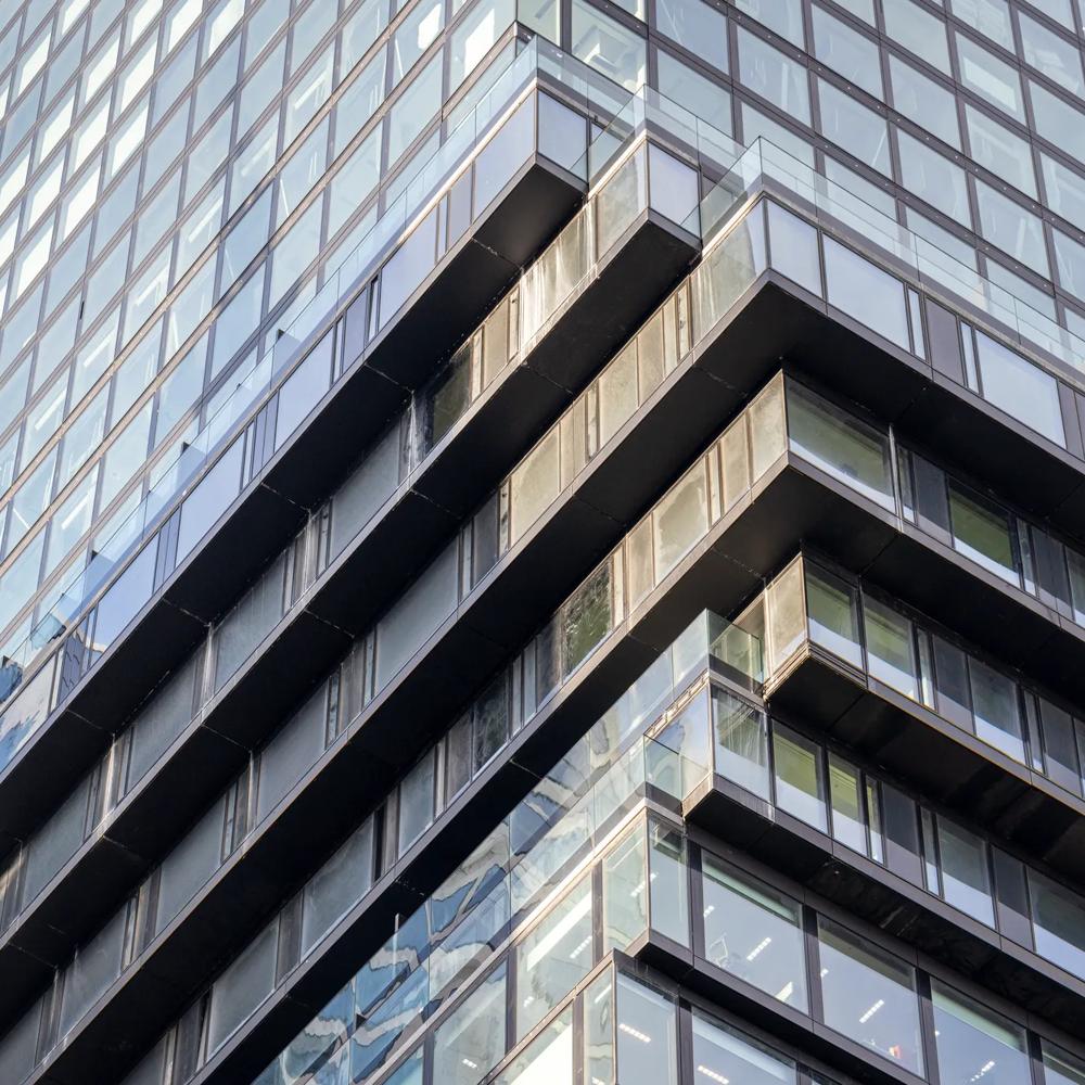 A modern high-rise building with a glass facade and offset balconies against a blue sky.