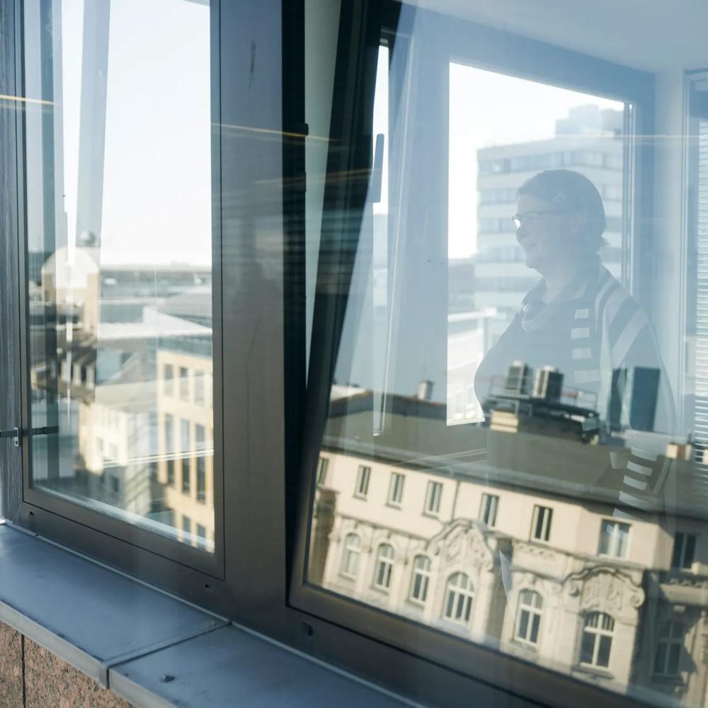 Reflexion einer Person in einem Fenster mit Blick auf städtische Gebäude im Hintergrund.