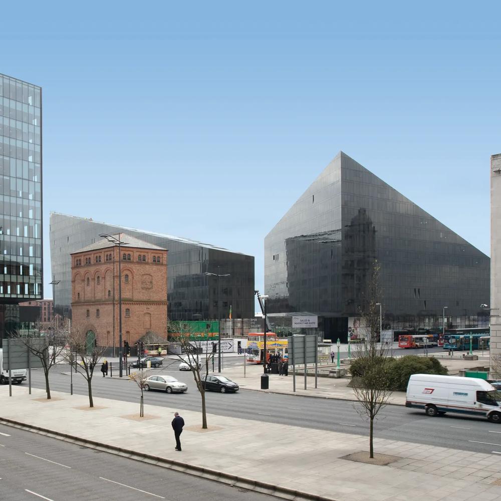 Moderne Glasgebäude und ein altes Backsteingebäude an einer belebten Straße bei klarem Himmel.