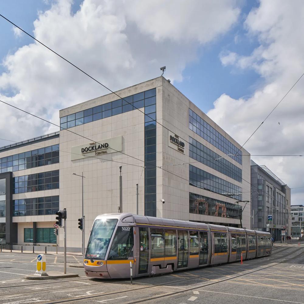 Eine Straßenbahn fährt vor einem modernen Bürogebäude unter bewölktem Himmel entlang.