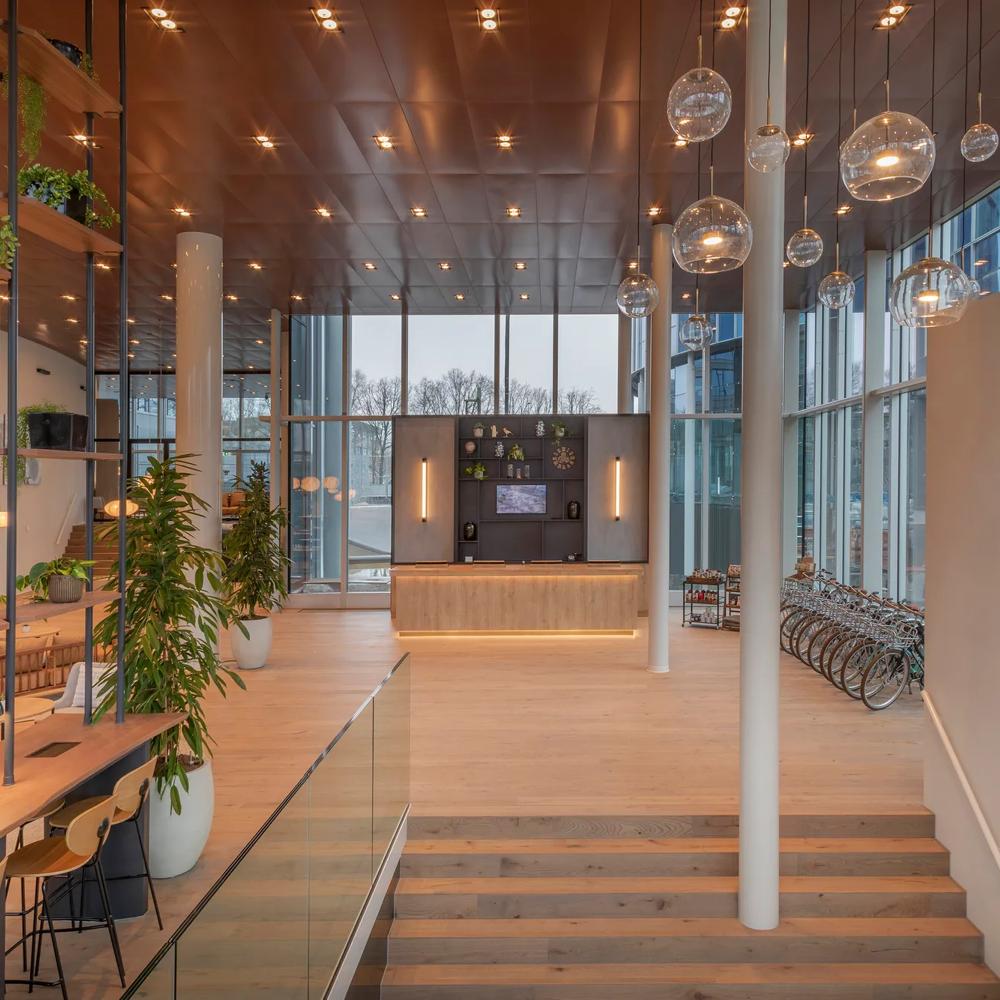 Ein modernes Foyer mit Holzdekor, Pflanzen, Treppen, hängenden Lampen und großen Fenstern.