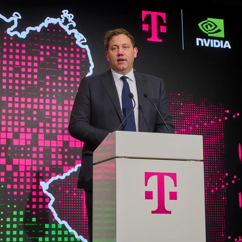 Ein Mann im dunklen Anzug spricht am Rednerpult mit Telekom-Logo. Im Hintergrund eine digitale Deutschlandkarte mit Telekom- und NVIDIA-Branding.