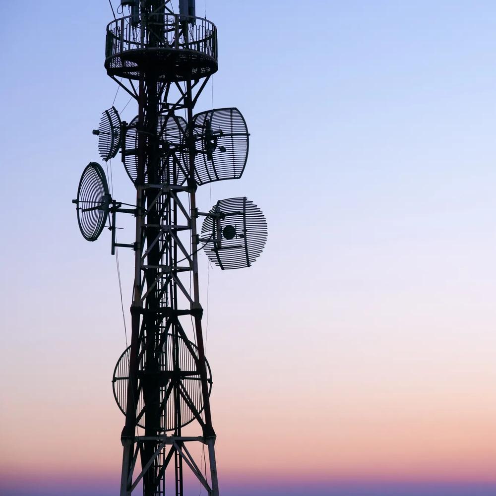 Ein Sendemast mit Antennen vor einem pastellfarbenen Sonnenuntergangshimmel.