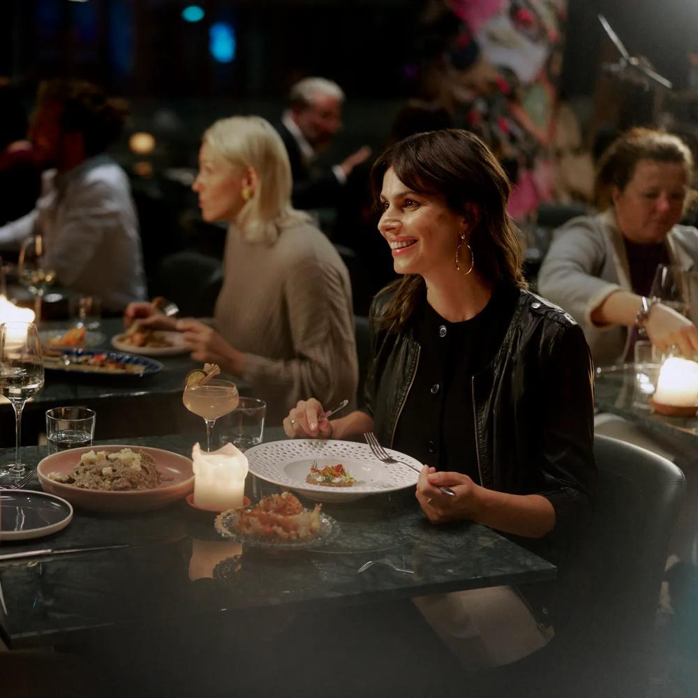 Zwei Frauen sitzen lächelnd bei Kerzenschein an einem Tisch in einem belebten Restaurant.