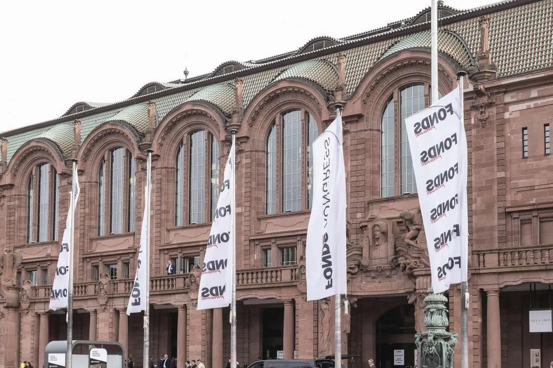 Exhibition stand with wooden walls, green moss, a screen and a wheel of fortune, decorated with pictures of buildings.