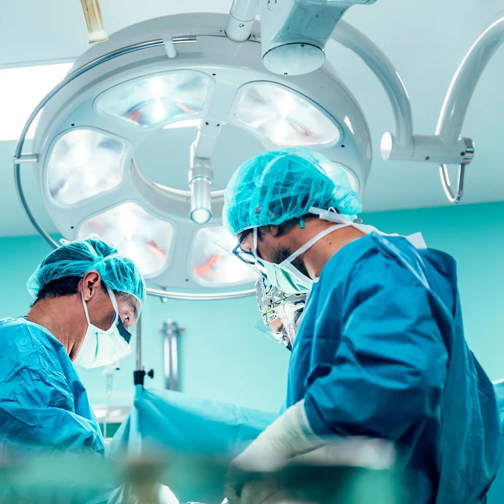 Chirurgen in OP-Kleidung arbeiten konzentriert unter hellem OP-Licht in einem Operationssaal.