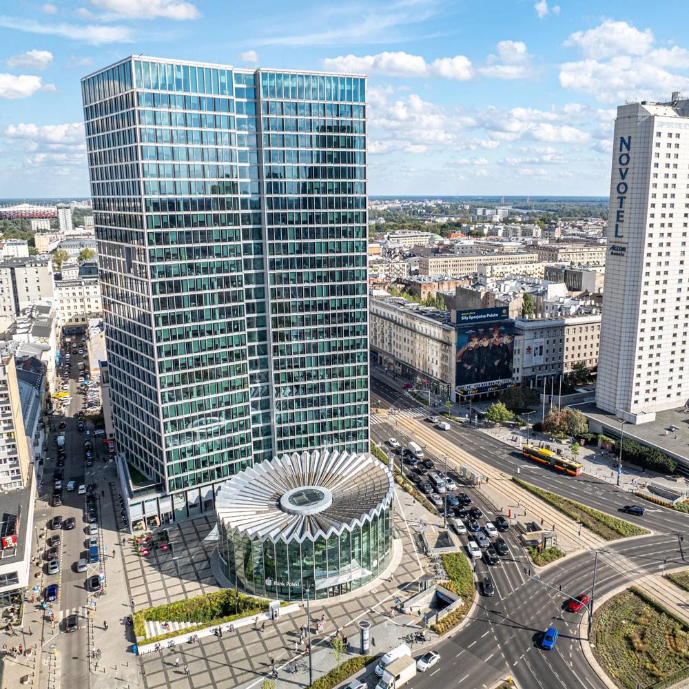 Zwei moderne Hochhäuser in einer Stadtlandschaft mit belebter Straßenkreuzung und blauem Himmel.
