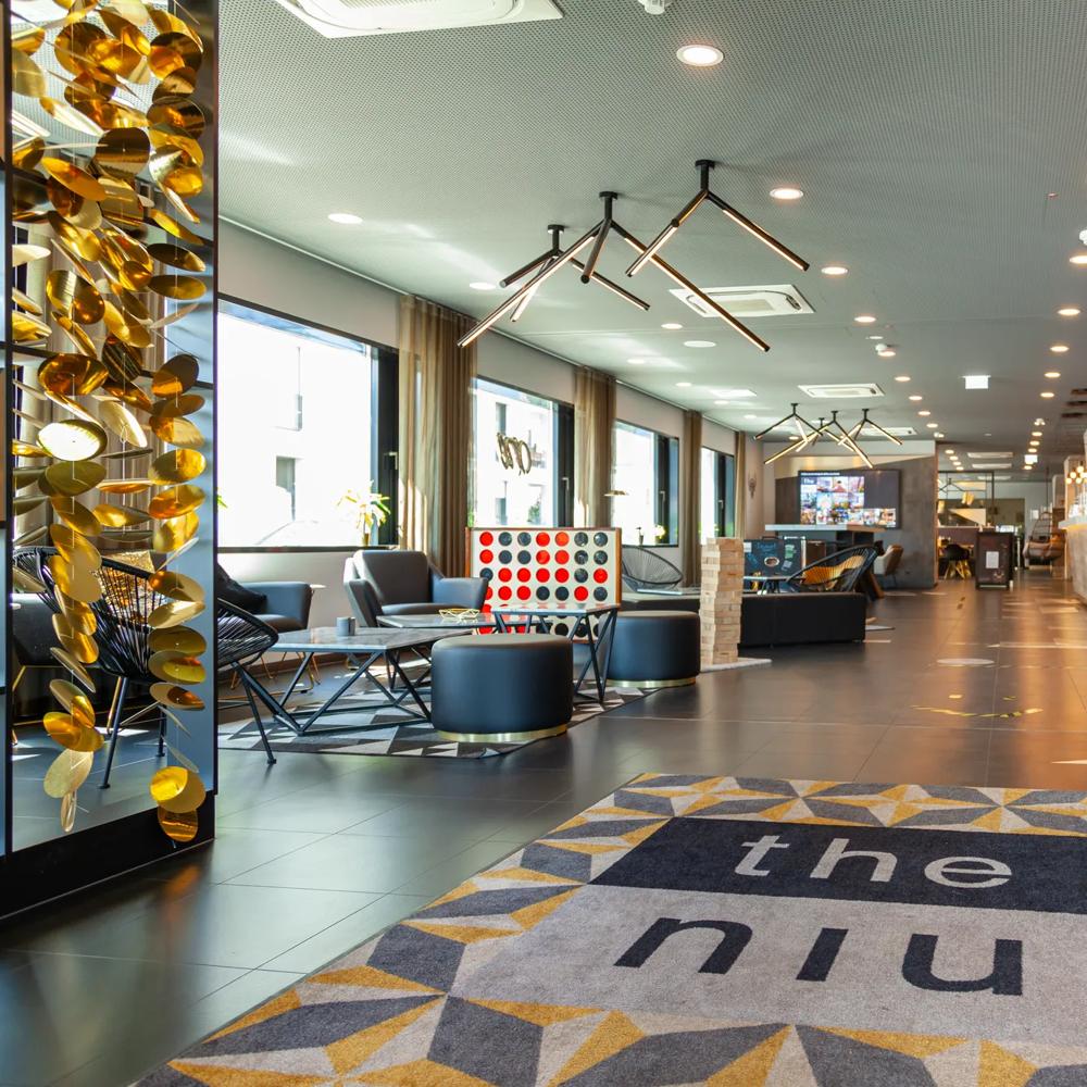 Moderne Hotellobby mit stilvollen Möbeln, großem Teppich mit "the niu" und dekorativen Lichtern.