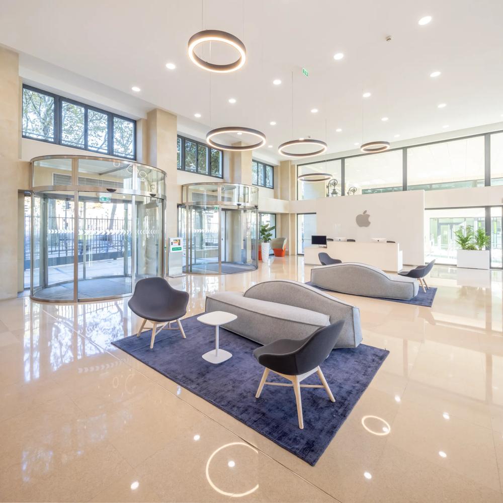 Heller Empfangsbereich mit modernen Möbeln, runden Lichtern und Glasdrehtüren.