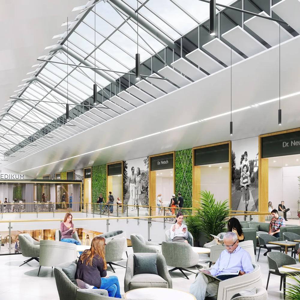 Menschen gehen durch ein modernes Einkaufszentrum mit Glasdach und grünen Wänden.