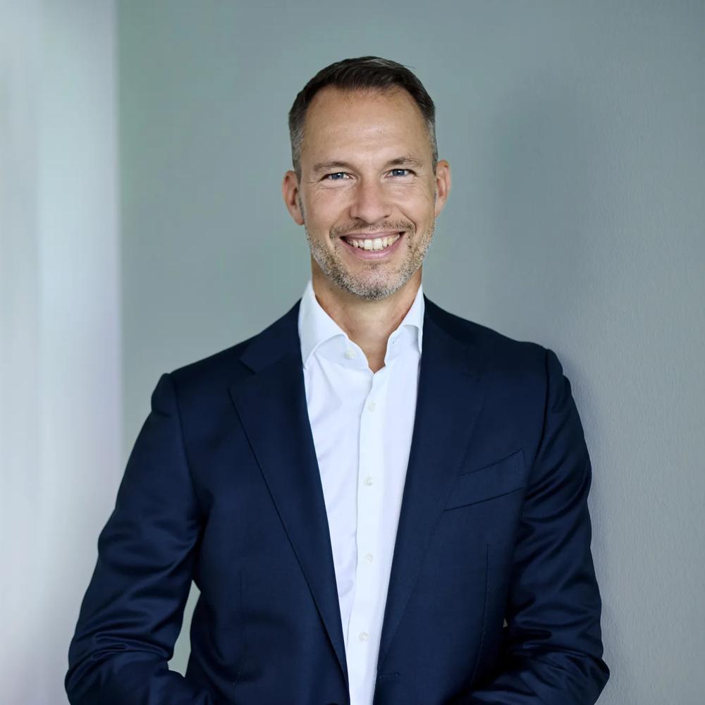 Michael Henn ist Global Head of Green Deal Infrastructure. Michael Henn lehnt gegen eine gruene Wand, neben ihm ist eine Metall-Skulptur.