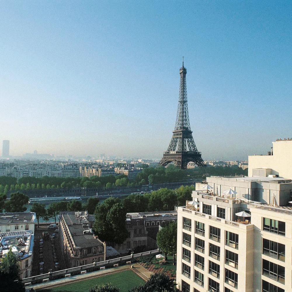 Der Eiffelturm ragt über Paris, umgeben von Gebäuden und grünen Bäumen bei klarem Himmel.