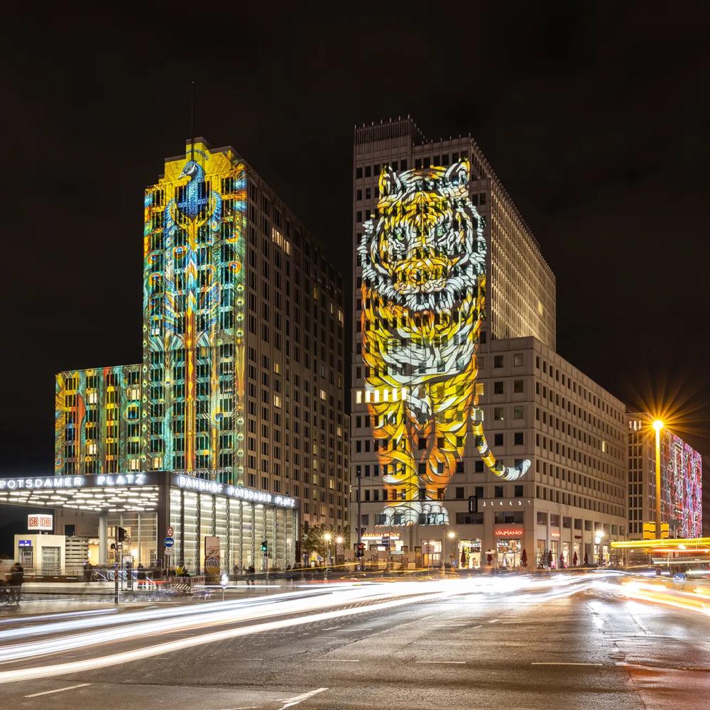 Ein leuchtender Tiger ist nachts auf ein hohes Gebäude projiziert, umgeben von Stadtlichtern.