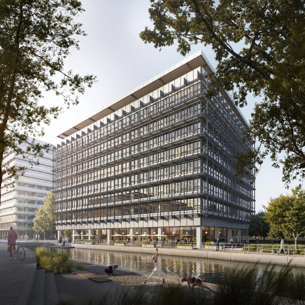 A modern, glazed office building by the water, surrounded by trees and people on a pavement.