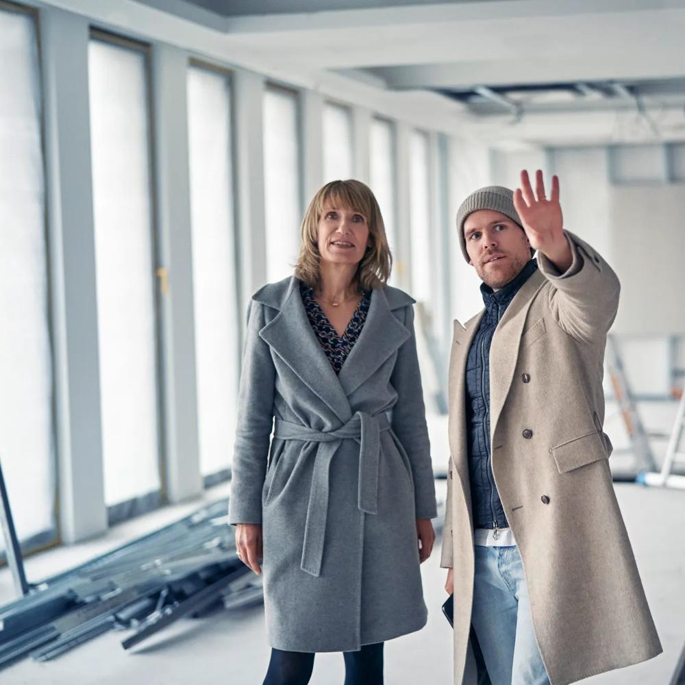 Eine Frau mit schulterlangem Haar trägt einen grauen Mantel und schaut nach oben.